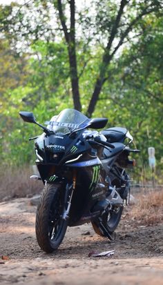 a motorcycle parked on the side of a dirt road in front of trees and bushes