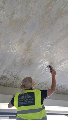 a woman in a yellow vest is painting a ceiling with white paint on the ceiling