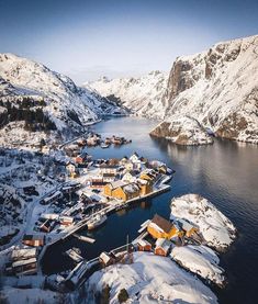 an aerial view of a small village in the middle of snow covered mountains and water