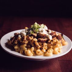 a white plate topped with macaroni and cheese covered in sauce on top of a wooden table