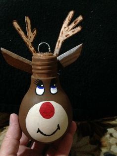 a hand holding a brown and white reindeer ornament with eyes on it's nose