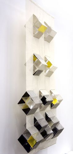 an abstract sculpture is hanging on the wall in front of a white wall with yellow and black shapes