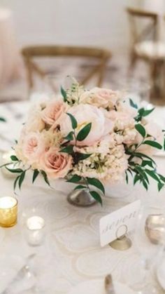 a centerpiece with flowers and greenery sits on a table at a wedding reception