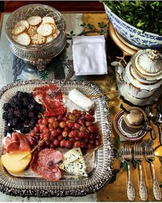 a platter of cheese, meats and fruit on a table with silverware