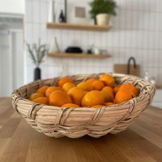 a wicker basket filled with oranges on top of a wooden table in a kitchen