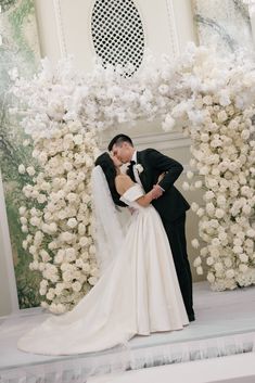 a bride and groom kissing in front of a floral arch at their wedding ceremony with white flowers