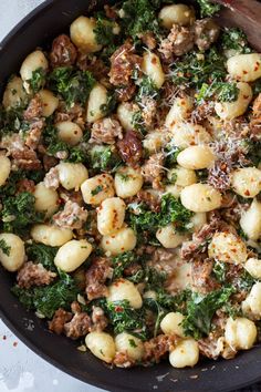 a skillet filled with pasta and spinach covered in meat, cheese and parmesan