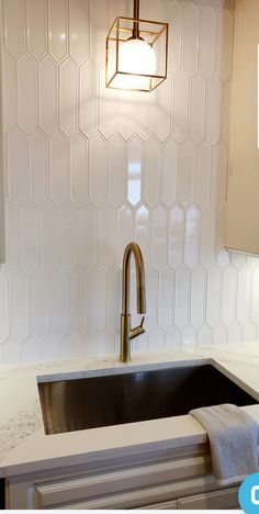 a kitchen sink under a hanging light in a white tile backsplash with hexagonal tiles