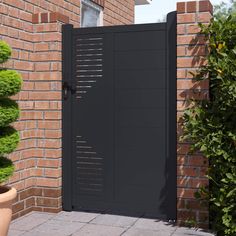 an open black gate in front of a brick wall and potted plant on the ground