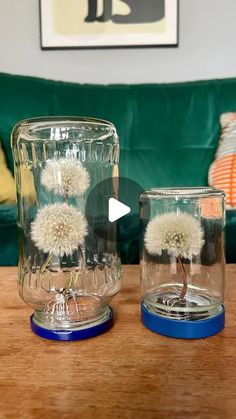 two glass vases with dandelions in them sitting on a table next to a couch