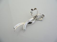 Overview:Offered for sale is a wonderful and very pretty Tiffany and Co. Sterling Silver Ribbon Brooch / Pin. The piece is made from bright and substantial Tiffany silver fashioned to look like a flowing bow / ribbon - very striking and pretty! In excellent condition, this piece is one that you will turn to very often to jazz up your wardrobe. It is no longer produced, and thus makes a great addition for any Tiffany collector. The piece has a perfectly working locking mechanism, and is fully hal Elegant Brooches With Decorative Bow For Anniversary, Elegant Anniversary Brooches With Decorative Bow, Elegant Anniversary Brooch With Decorative Bow, Elegant Silver Heart Brooches, Elegant Silver Heart-shaped Brooches, Elegant Silver Heart Brooch, Elegant Silver Heart-shaped Brooch, Elegant Silver Brooch With Bow, Silver Brooch With Ribbon For Gifts