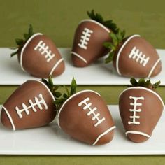 four chocolate covered strawberries with footballs on them sitting on a white platter