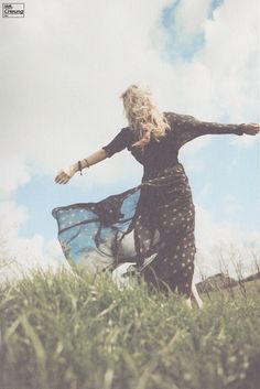 a woman is standing in the grass with her arms spread out and she is wearing a dress