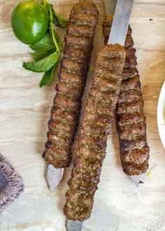 two skewers of meat sitting on top of a cutting board next to a knife