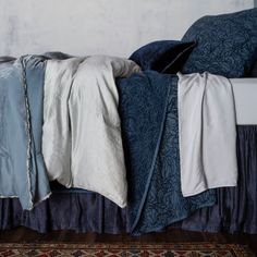 a bed with blue and white sheets on top of it, next to a rug