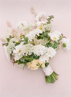 a bouquet of white and yellow flowers on a light pink background with greenery in the middle