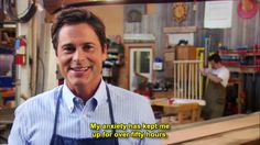 a man with an apron on standing in front of a table and talking to someone