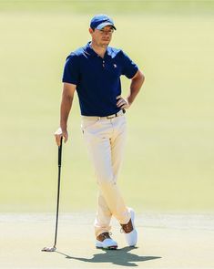 a man in blue shirt and white pants holding a golf club while standing next to a green