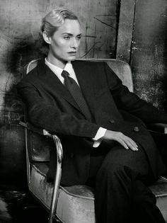 a black and white photo of a woman in a suit sitting on a chair with her legs crossed