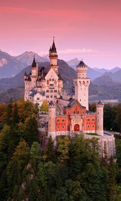 an old castle sits on top of a hill surrounded by trees and mountains in the background