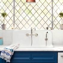 a kitchen sink with blue cabinets and white counter tops in front of a large window