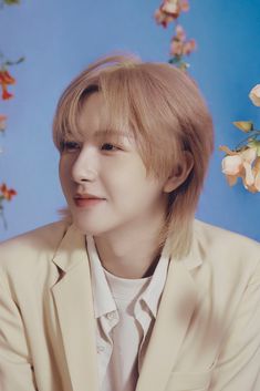 a man with blonde hair wearing a beige suit and white shirt sitting in front of flowers