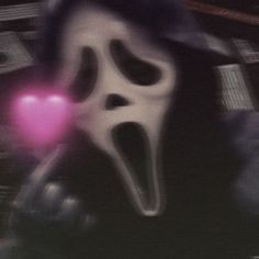 a person wearing a ghost mask holding a pink heart in their hand and looking at the camera