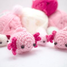 crocheted pink and white animals sitting next to balls of yarn on a table