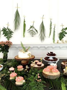 a table topped with cakes and cupcakes covered in frosting surrounded by greenery