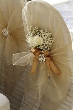 two white roses and baby's breath are tied to the back of some chairs