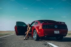 a woman sitting on the back of a red car in the middle of an empty road