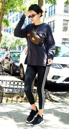 a woman in black shirt and leggings standing on sidewalk next to tree with handbag