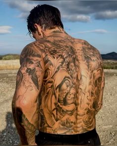 the back of a man with tattoos on his arms and shoulder, standing in front of an open field