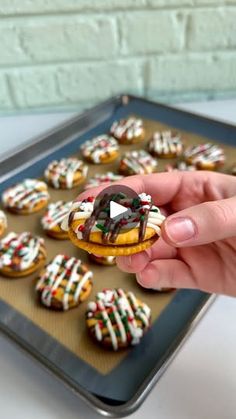 a person holding a donut in front of a tray of decorated doughnuts