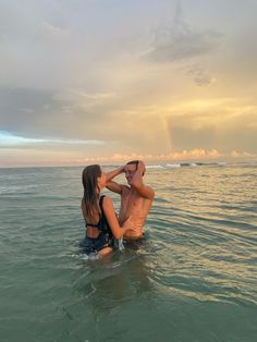 a man and woman are in the water with a rainbow in the sky behind them