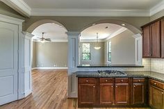 an empty kitchen with wood floors and white walls, along with arched doorways that lead into the living room