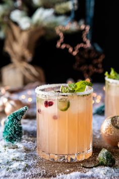 two glasses filled with drinks sitting on top of snow covered ground next to christmas decorations