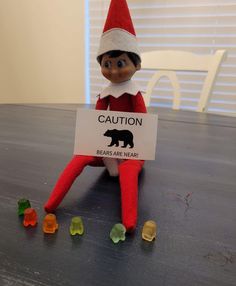 an elf sitting on top of a table holding a sign that says caution bears are near