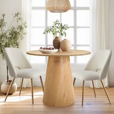 a round wooden table with two chairs and a vase on it in front of a window