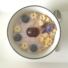 a bowl filled with cereal and fruit on top of a white table next to a spoon