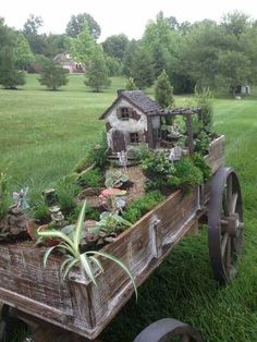 an old wooden wagon filled with lots of plants and small houses in the back yard