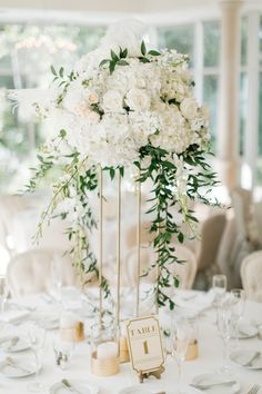 a table with white flowers and greenery in tall vases on top of it