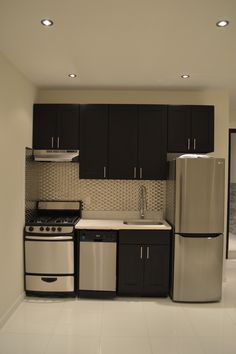 a kitchen with black cabinets and white tile flooring, stainless steel appliances and refrigerator