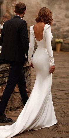 a woman in a white dress walking next to a man in a black tuxedo