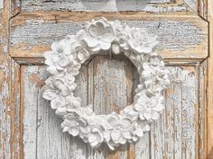 a white wreath hanging on the side of an old wooden door with peeling paint and chipped paint