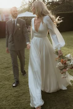 a bride and groom walking in the grass holding hands at their outdoor wedding ceremony on a sunny day