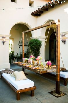 an outdoor dining area with white cushions and wooden tables, hanging lights and potted plants