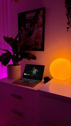 a laptop computer sitting on top of a white dresser next to a plant in a vase