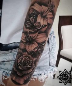 a black and white tattoo with flowers on the arm, butterflies flying over it in the background