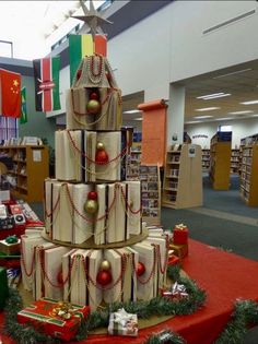 a christmas tree made out of wrapped presents on a table in a library filled with books